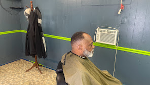 Man getting a haircut in a barbershop with a fan on the wall.